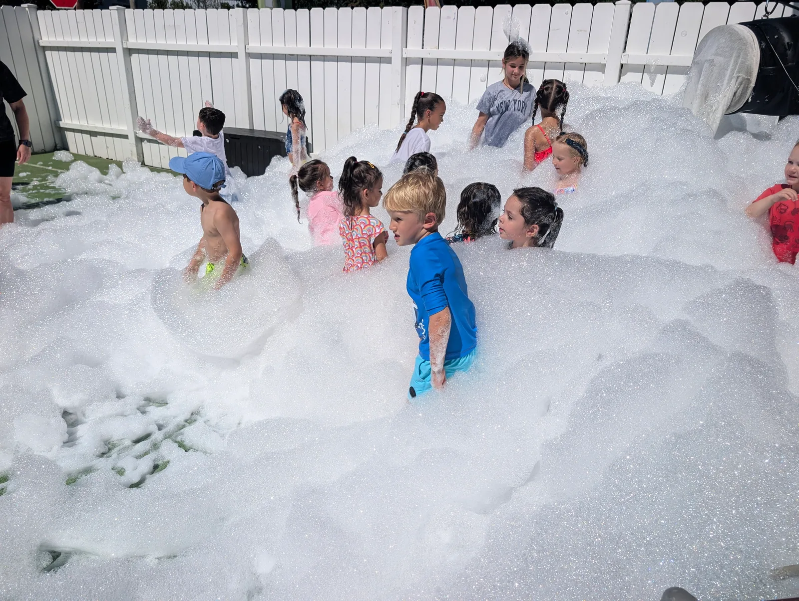 Children playing in white foam in a fenced outdoor area